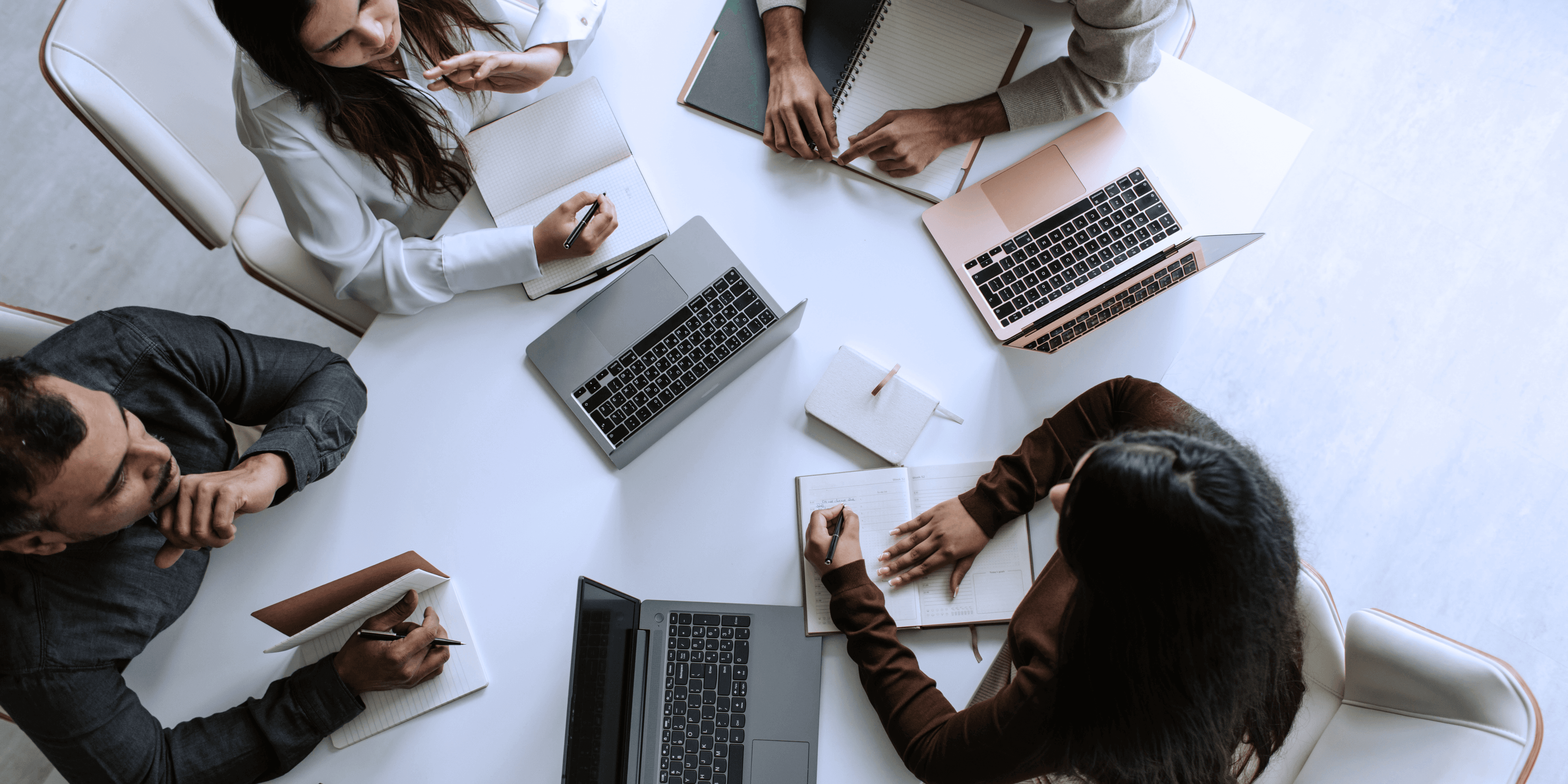 Professionals in discussion at a conference table with laptops.
